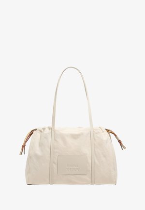 Beige fabric tote bag with dual handles, gathered top, and embossed logo patch. Features decorative cord accents on the sides.