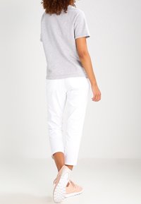 Grå kortärmad t-shirt med rund halsringning, ihopparad med vita cropped byxor. Skorna är ljusrosa sneakers med vita sulor.