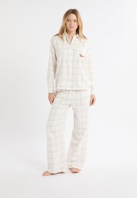 Komplet piżam w kratę w kolorze kremowym z jasnopomarańczowymi liniami; posiada zapinaną na guziki górę z kieszenią na piersi i haftowanym detalem. Spodnie o luźnym kroju.