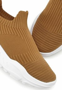 Scarpe sportive slip-on in tessuto a maglia marrone con texture a coste, suola in gomma bianca e design della punta liscia e arrotondata.