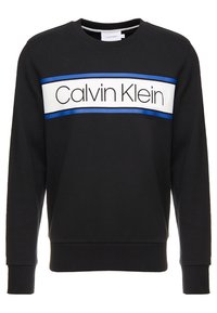 Czarna bluza z białym poziomym pasem z niebieskimi akcentami i logo "Calvin Klein". Mankiety i dół bluzy są ściągane, co dodaje tekstury.