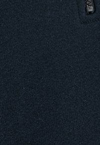 Tejido azul marino con una textura suave y cierre de cremallera. El material parece blando y ligeramente elástico, sin patrones visibles.