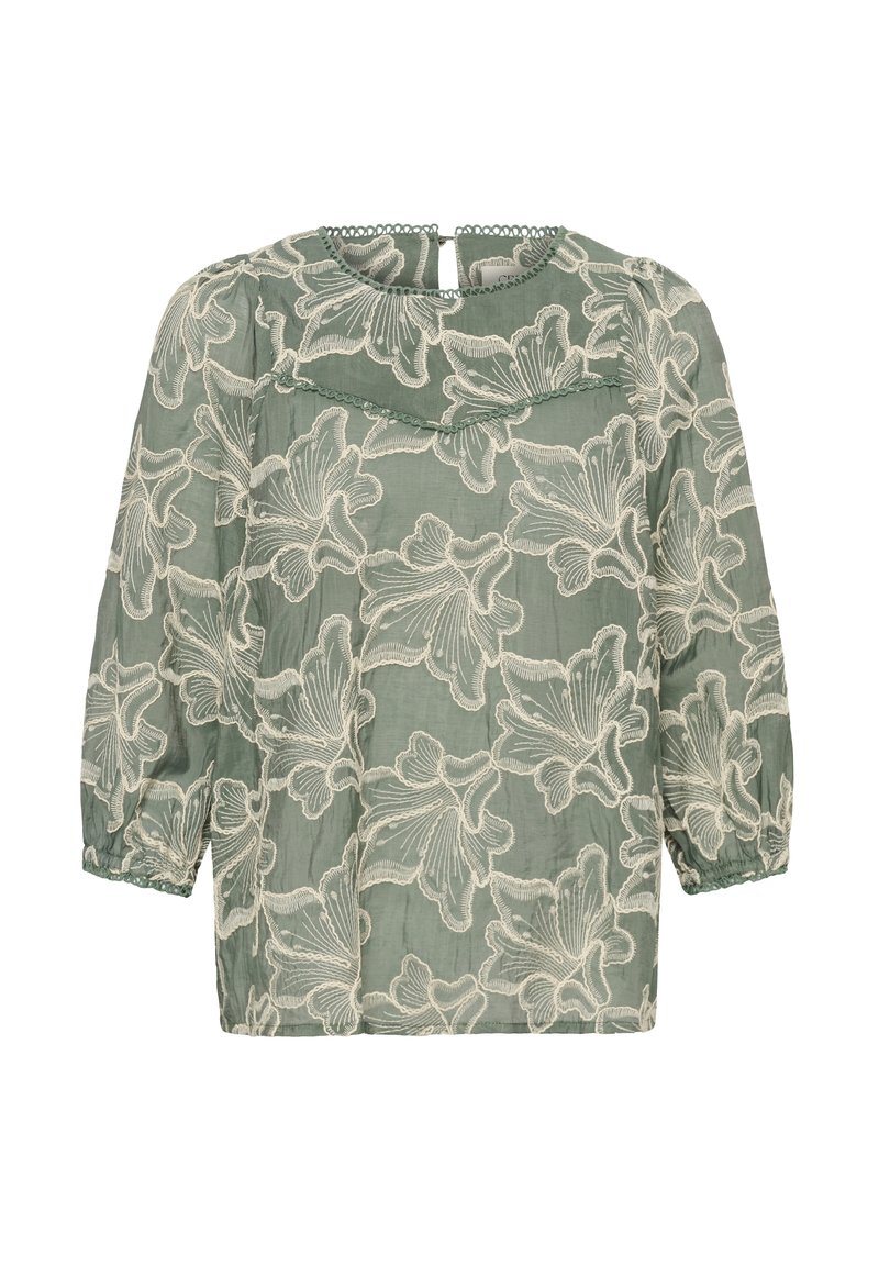 Blouse verte avec superposition de dentelle florale blanche, manches longues bouffantes avec poignets élastiques et petite fermeture bouton en trou de serrure au dos de l'encolure.