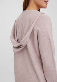 Ljusrosa huva-tröja med en mjuk textur, med en lös passform och rundad halsringning; synlig sömdetalj på baksidan.