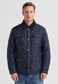 Marineblaue gesteppte Jacke mit einem schwarzen Wildlederkragen, zwei Brusttaschen und Druckknöpfen, entworfen für Wärme und eine strukturierte Passform.