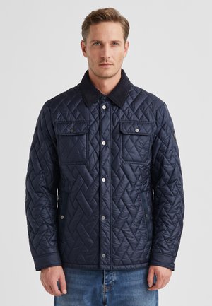 Marineblaue gesteppte Jacke mit einem schwarzen Wildlederkragen, zwei Brusttaschen und Druckknöpfen, entworfen für Wärme und eine strukturierte Passform.