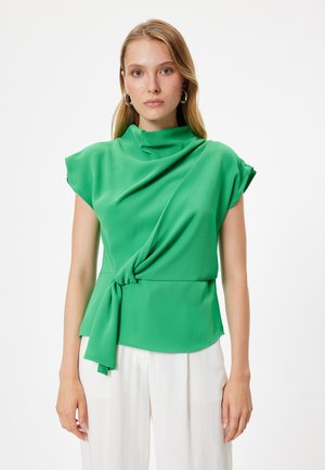 Blusa verde con scollatura drappeggiata e maniche corte, dotata di un dettaglio legato in vita. Tessuto liscio e leggero su uno sfondo semplice.