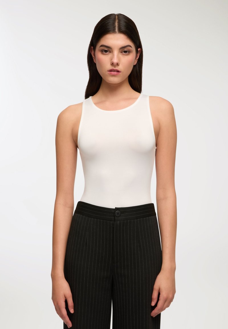 Biały bezrękawnik z okrągłym dekoltem w połączeniu z czarnymi spodniami w paski, z zapięciem na guziki i dopasowanym krojem.