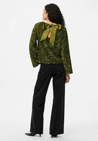 Top color verde oliva con paillettes, maniche lunghe e un fiocco sul retro, abbinato a jeans neri a vita alta e svasati.