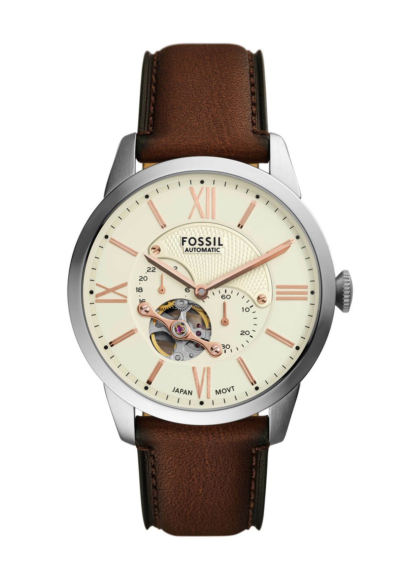 Cinturino in pelle marrone, cassa in acciaio inossidabile argentato, quadrante crema con dettagli in oro rosa, movimento visibile e indicatori in numeri romani.