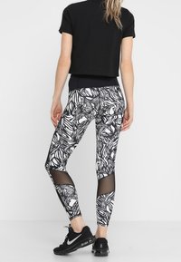 T-shirt nero corto abbinato a leggings aderenti neri e bianchi con motivi, featuring pannelli in rete. Sneakers nere Nike completano l'outfit.