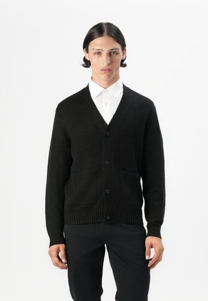 Black cardigan with a V-neck, ribbed cuffs, and hem. Features two front pockets and button closure. Worn over a white shirt.