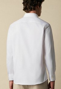 Witte langemouwen blouse van soepel stof, met een klassieke kraag, knoopmanchetten en een rechte zoom. Achteraanzicht weergegeven.