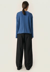 Blå strikket sweater med en afslappet pasform og rund hals, parret med løse sorte bukser. Sweateren har en detalje med en bagsøm og en blød tekstur.