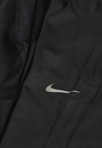 Bañadores deportivos negros hechos de un tejido suave, con un logo plateado de Nike y costuras en contraste a lo largo de las costuras.