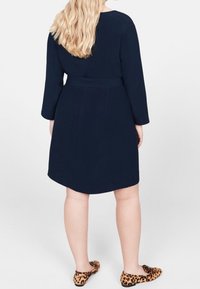 Meriini sininen, pitkähiha dressi, jossa on vyötaroitu vyötärö ja kaareva helma. Yhdistetty leopardikuvioisiin tasapohjaisiin kenkiin. Sujuva pinta ja minimalistinen muotoilu.