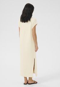 Rochie maxi de culoare crem, cu mâneci scurte, fante laterale și o siluetă lejeră. Material moale și ușor care se așază până la glezne.