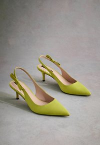 Talons slingbacks verts avec un bout pointu et un petit nœud sur le talon. Texture lisse et talon aiguille slim.