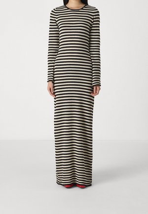 Langes, gestricktes Kleid mit schwarzen und cremefarbenen horizontalen Streifen, rundem Ausschnitt und langen Ärmeln; kombiniert mit roten Schuhen.