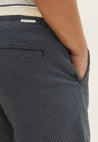 Navyfarbene Stoffhosen mit einem strukturierten Muster aus kleinen weißen Rauten, ausgestattet mit einer Seitentasche und einem gewebten beigen Gürteldetail.