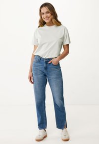 Světle zelené tričko spárované s džínami středního praní, které mají postranní rozparky. Bílé tenisky dokončují ležérní outfit.