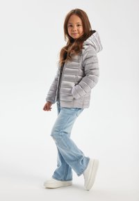 Sølv pufferjakke med hætte, der har vandret quilting, parret med lyseblå, let slidte jeans og hvide platform sneakers.
