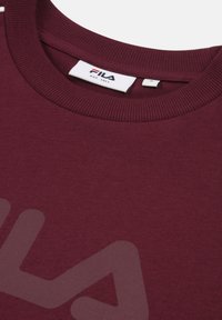 Sweatshirt bordeaux avec un col rond côtelé, texture douce et un grand logo en relief d'une teinte plus claire sur le devant.