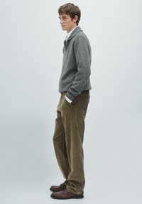 Šedý pletený svetr s límcem na zip, v kombinaci se světle hnědými kordovými kalhotami. Hnědé boty dotvářejí outfit. Jednoduchý, texturovaný design.