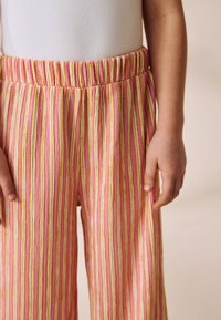 Pantalon rayé rose et jaune avec une ceinture élastique, présentant une texture verticale. Vue en gros plan mettant en valeur le tissu et la coupe.