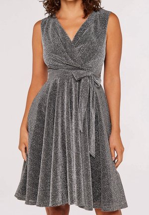 Robe cache-cœur pailletée argentée sans manches avec col en V et ceinture à la taille, longueur genoux, portée par une femme aux cheveux bouclés.