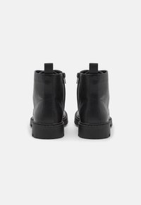 Black leather ankle boots with a smooth texture, featuring a zip closure and pull tab at the back, complemented by a chunky sole.