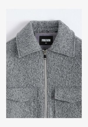 Veste grise texturée avec fermeture éclair, grand col et deux poches avant. L'étiquette indique "FRILIVIN" avec les informations de taille en dessous.