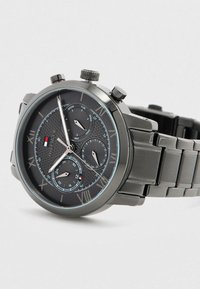 Orologio da polso in metallo nero con numeri romani, tre quadranti secondari per giorno, data e ora 24 ore, e un bracciale in metallo a maglie.