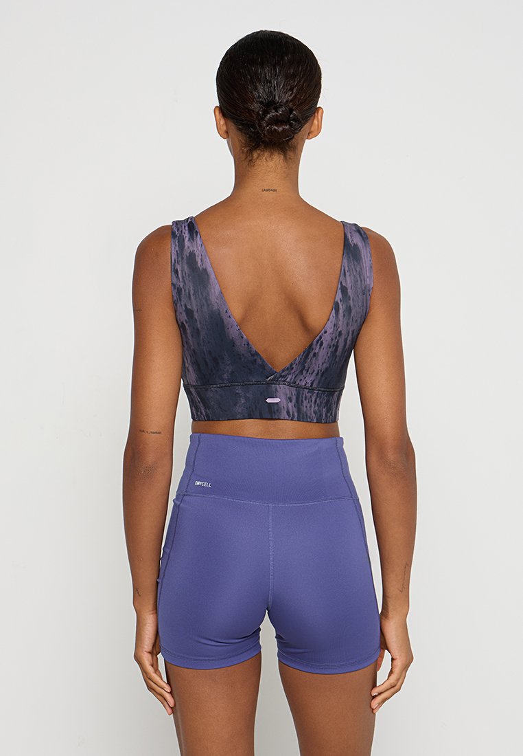 Reggiseno sportivo viola con design a V sul retro e motivo distintivo; abbinato a short a vita alta in un viola uniforme.