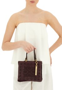Borsa a mano in pelle bordeaux con motivo floreale in rilievo, due manici marroni e un'etichetta in tonalità oro. Design compatto e rettangolare.
