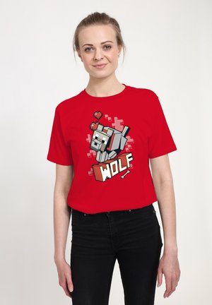 Czerwona bawełniana koszulka z grafiką w stylu pixel art przedstawiającą wilka, grafiką serc oraz wyrazem "WOLF" w pogrubionej czcionce. Noszone są czarne dżinsy.