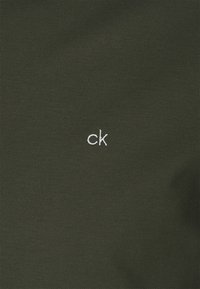 Tissu vert foncé à surface texturée affichant un petit logo blanc "ck" dans le coin inférieur droit.