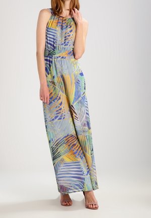 Woman wearing a sleeveless, sleeveless, floor-length dress with a multicolored abstract leaf pattern and open-toe high-heeled sandals.