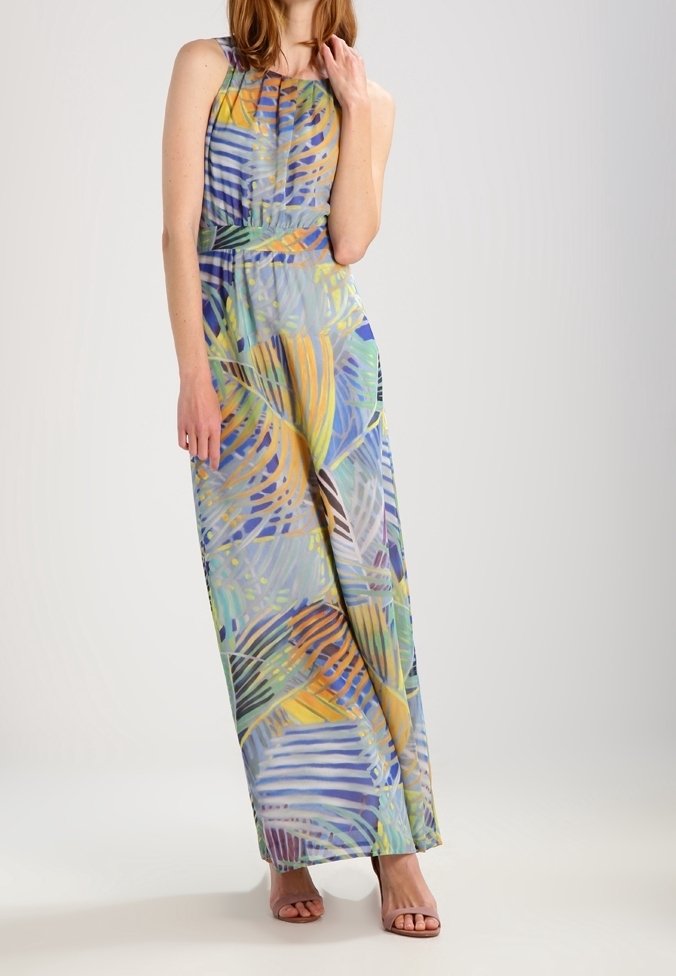 Femme portant une robe longue sans manches avec un motif abstrait de feuilles multicolores et des sandales à talons ouverts.