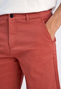Pantalons de couleur rouille en tissu mélangé coton, avec une coupe slim, des poches latérales et une fermeture à bouton à la taille.