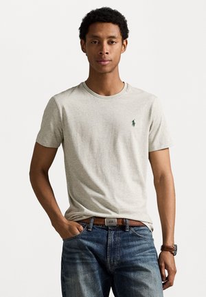 Grå bomulds t-shirt med rund halsudskæring, prydet med et lille grønt logo. Båret med denim jeans og et brunt bælte.