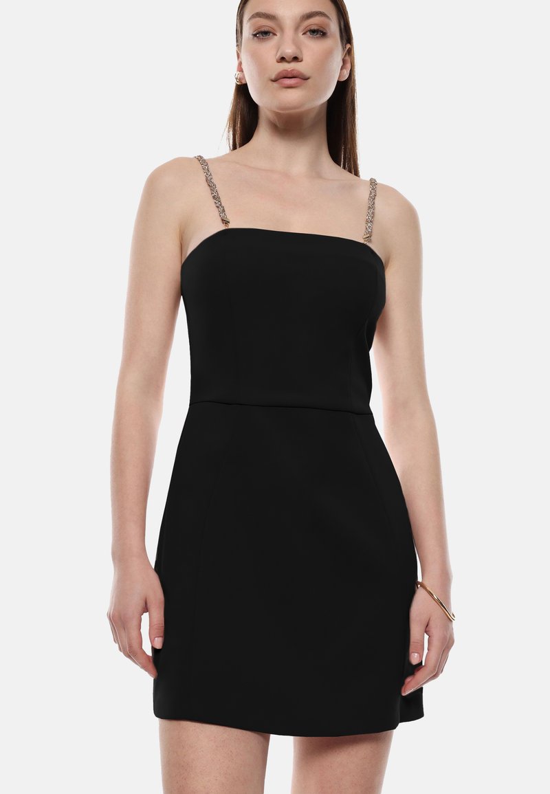 Miniabito nero con scollatura dritta, sottili spalline decorative e silhouette aderente. Tessuto liscio con dettagli minimi.