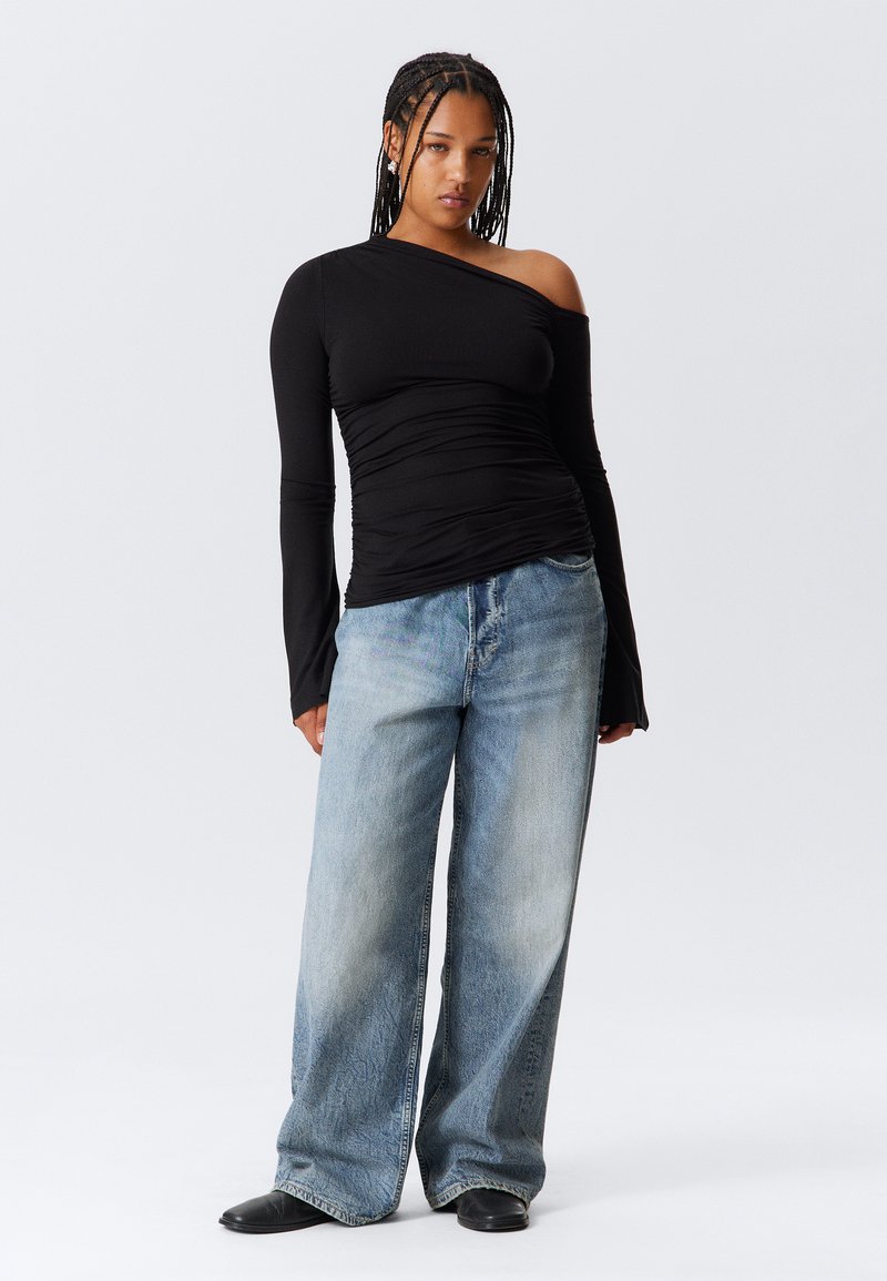 Top nero a spalla unica con manica lunga e texture arricciata abbinato a jeans in denim azzurro chiaro, a vestibilità ampia. Tessuto liscio, gamba larga.