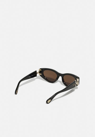 Schwarze Sonnenbrille mit braunen Gläsern, Katzenaugenform, glänzende Oberfläche, goldene Akzente an den Scharnieren und abgeschrägte schwarze Bügel mit Logodetail.