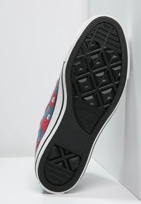 Semelle extérieure en caoutchouc noir avec un motif de bande de roulement, semelle intermédiaire blanche, et tige en laine colorée mêlant des tons de bleu et de rouge avec des éléments argentés.