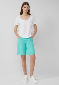 T-shirt blanc à col en V associé à un short turquoise mi-cuisse. Le short présente des ourlets roulés et des poches avant. Porté avec des baskets blanches.
