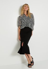 Jupe crayon noire avec une fente sur le côté, associée à un blouse en dentelle imprimée léopard avec des manches bouffantes et des boutons sur le devant.