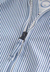 Gros plan d'un tissu rayé bleu et blanc avec une fermeture éclair en plastique blanc partiellement fermée et une languette en tissu.