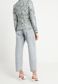 Blazer con un diseño de estampado de leopardo azul y blanco, combinado con jeans gris claro y sandalias de tacón blancas. La tela parece tener textura.