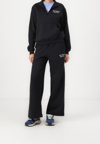 Zwarte sweatshirt met halve rits, kangoeroezak en logo; gecombineerd met loszittende zwarte sweatpants met een bijpassend logo.